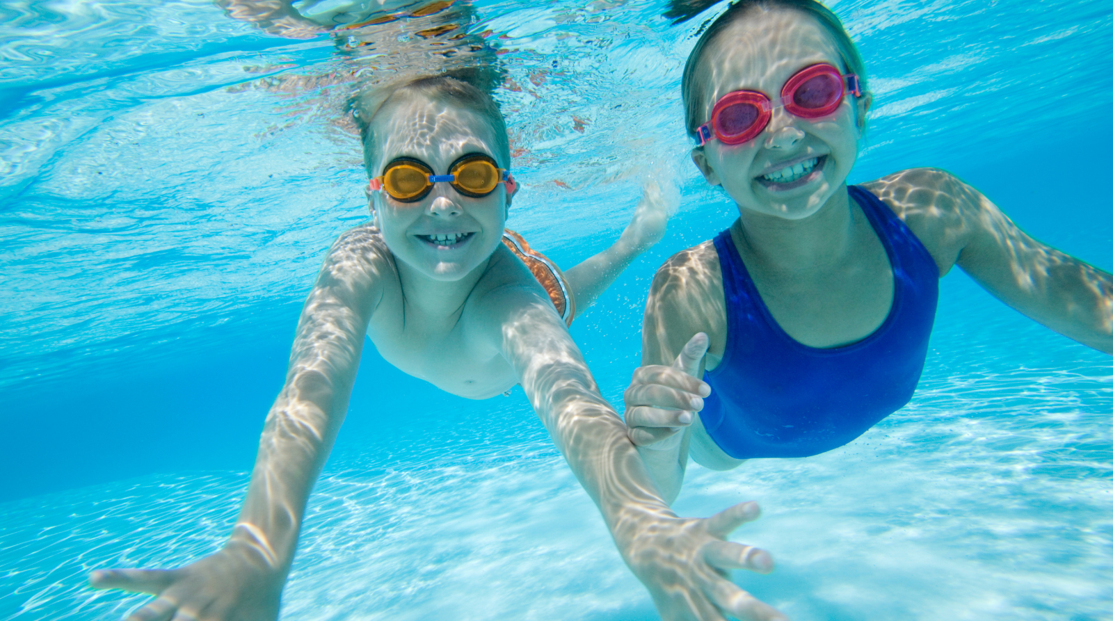 Two smiley children swimming underwater swim up to the camera Two smiley children swimming underwater swim up to the camera