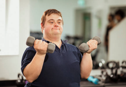Young man with Downs Syndrome smile whilst lifting dumbells Young man with Downs Syndrome smile whilst lifting dumbells