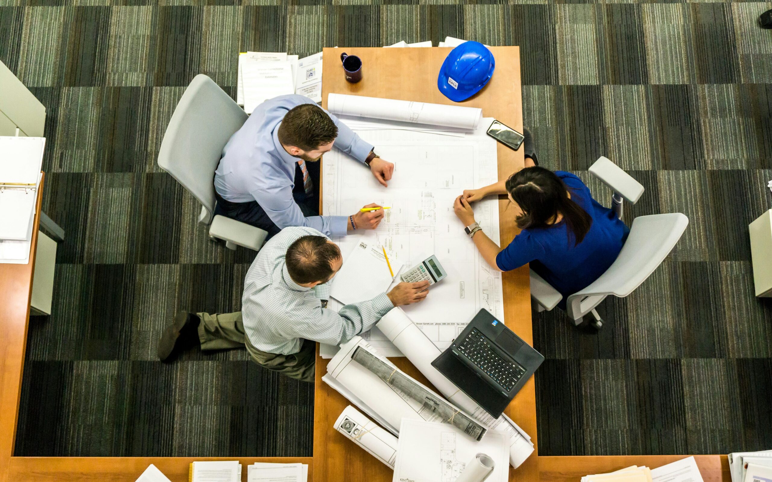 Construction Team working around a desk The photo shows several contractors collaborating on a project over a blueprint plan of a building site.