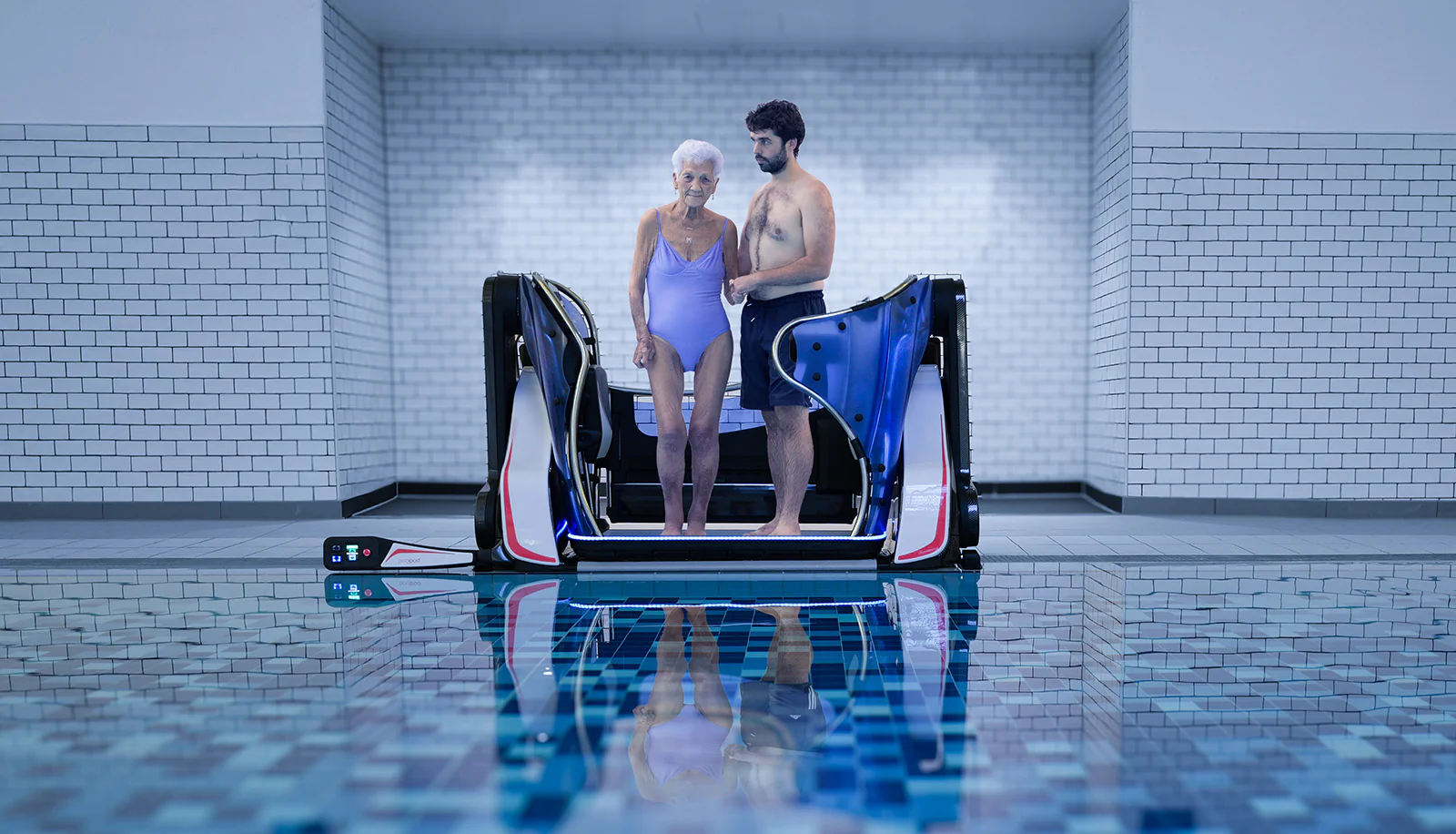 Image of an elderly lady being helped by a male to use a Pool Pod - a machine that helps give access to disabled people into a swimming pool