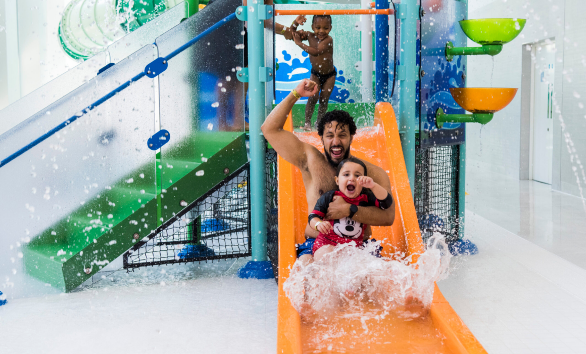 Adult and small child on small water slide in fun splash area